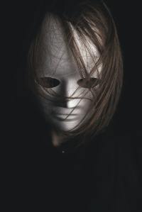 "The Strangers" - image shows a person with long brown hair falling over a white mask that is covering their face.