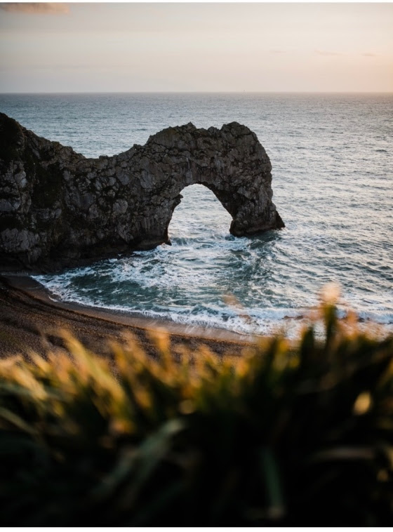 image shows a rock formation jutting out into the ocean with a large arch formed in it.