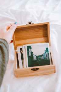 Image shows a person's hand holding open the lid to a wooden box filled with old photographs.
