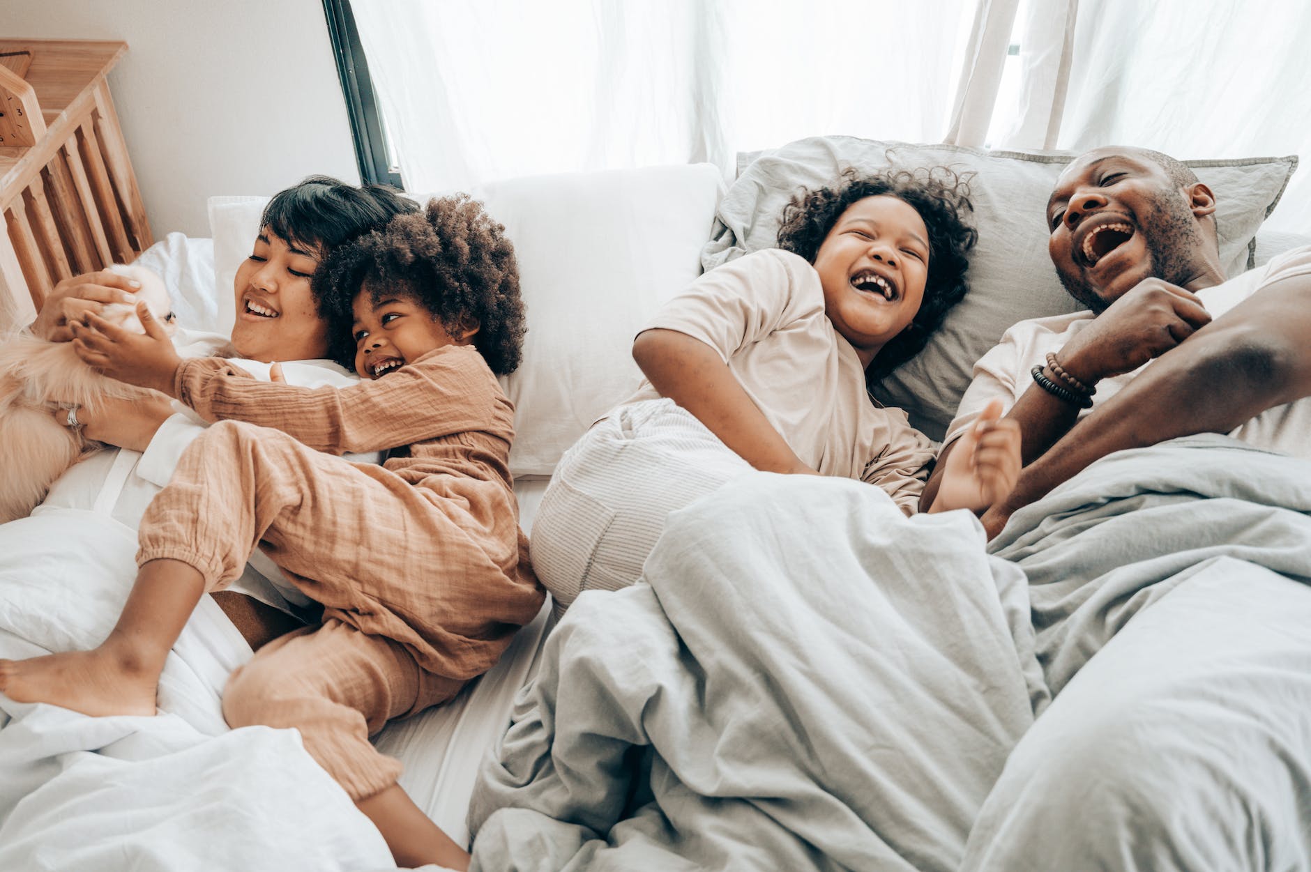 a family of four--father, mother, and two children--all laughing in a bed together