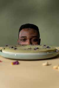 Image shows a man peaking above a table with a pie sitting on it. Only above his nose can be seen.