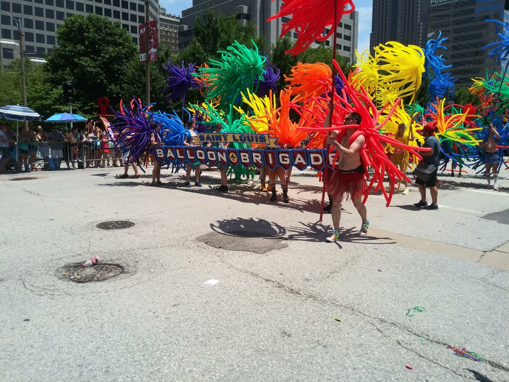 an exhibit of St. Louis Pride Parade 2019--people marching with large, colorful balloons leading with a banner reading "Balloon Brigade"