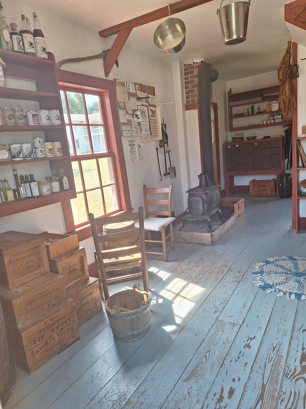 Another view of the inside of the General Mercantile with shelves containing jars and bottles of various food and liquids and an old wood stove in the corner of the room.