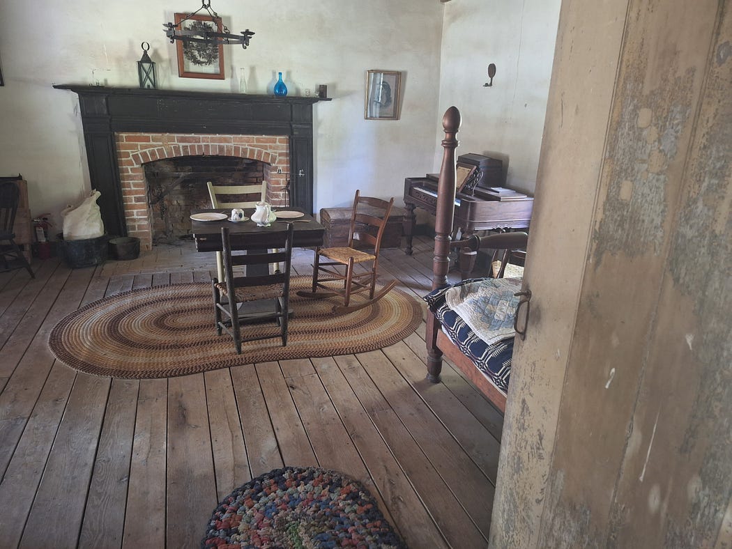 Inside of the tavern with a fireplace, table and chairs, and an old upright piano.